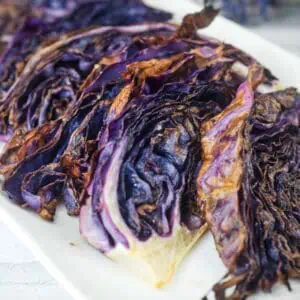 Sliced roasted purple cabbage arranged on a white rectangular plate, showing charred and crispy edges.