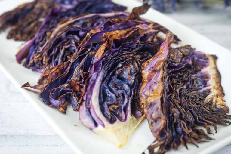 Sliced roasted purple cabbage arranged on a white rectangular plate, showing charred and crispy edges.