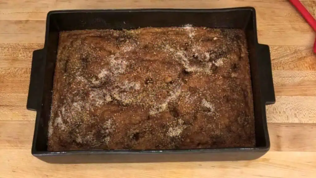 A rectangular baking pan filled with a baked coffee cake topped with a cinnamon and sugar mixture, resting on a wooden countertop.