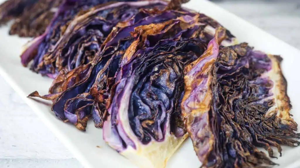 Slices of roasted purple cabbage with charred edges are arranged on a white rectangular plate.
