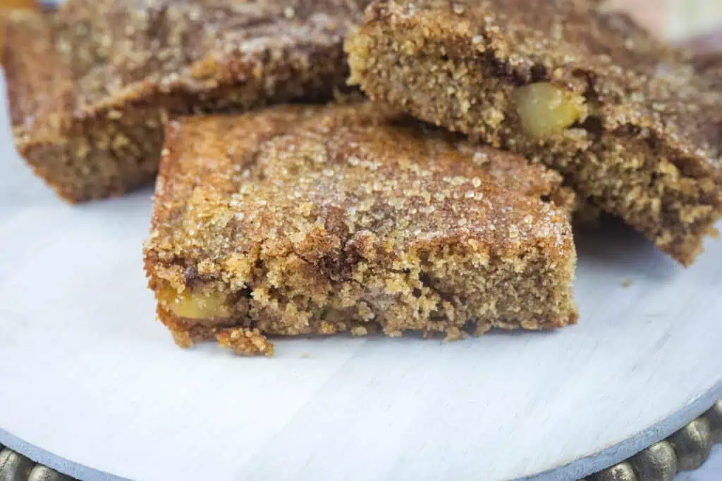 Close-up of three brown sugar-coated blondie bars with visible apple chunks, stacked on a light-colored surface.