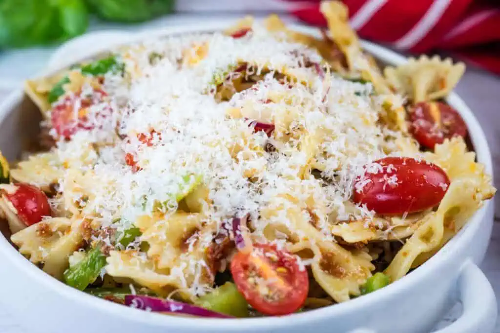 A bowl of bowtie pasta salad with cherry tomatoes, green vegetables, and shredded cheese on top.