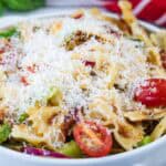 A bowl of bowtie pasta salad with cherry tomatoes, green vegetables, and shredded cheese on top.