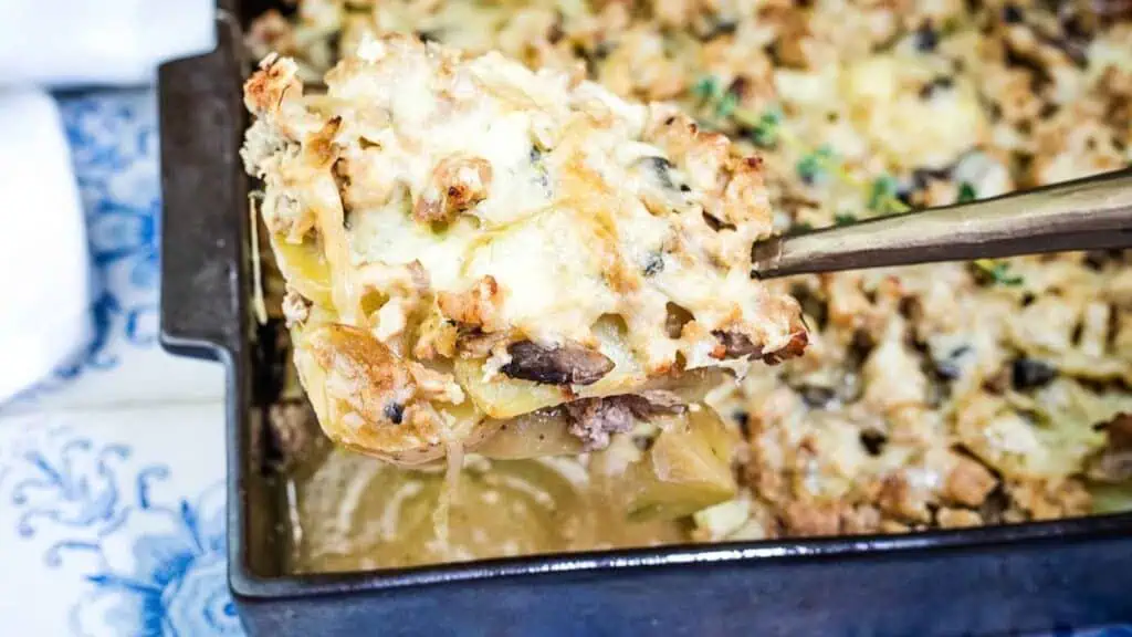 A metal spatula lifts a serving of baked casserole with a golden cheese topping from a rectangular baking dish.