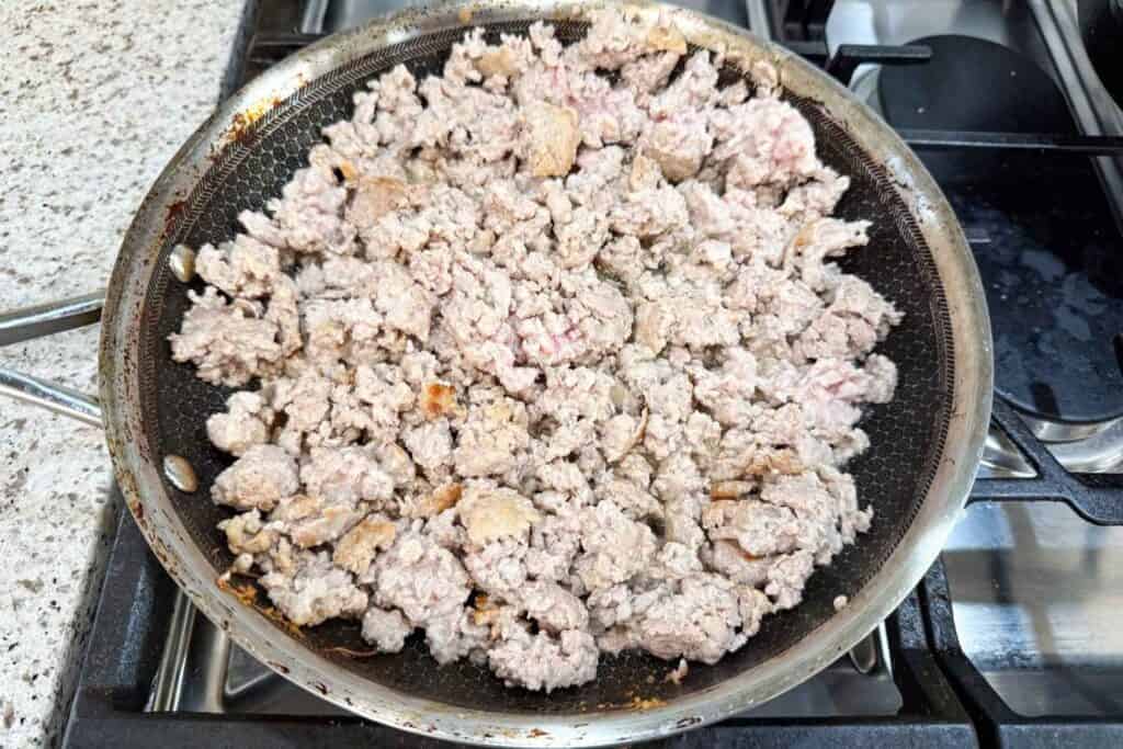 Ground meat cooking in a frying pan on a stovetop, with some pieces browned and others still light pink.