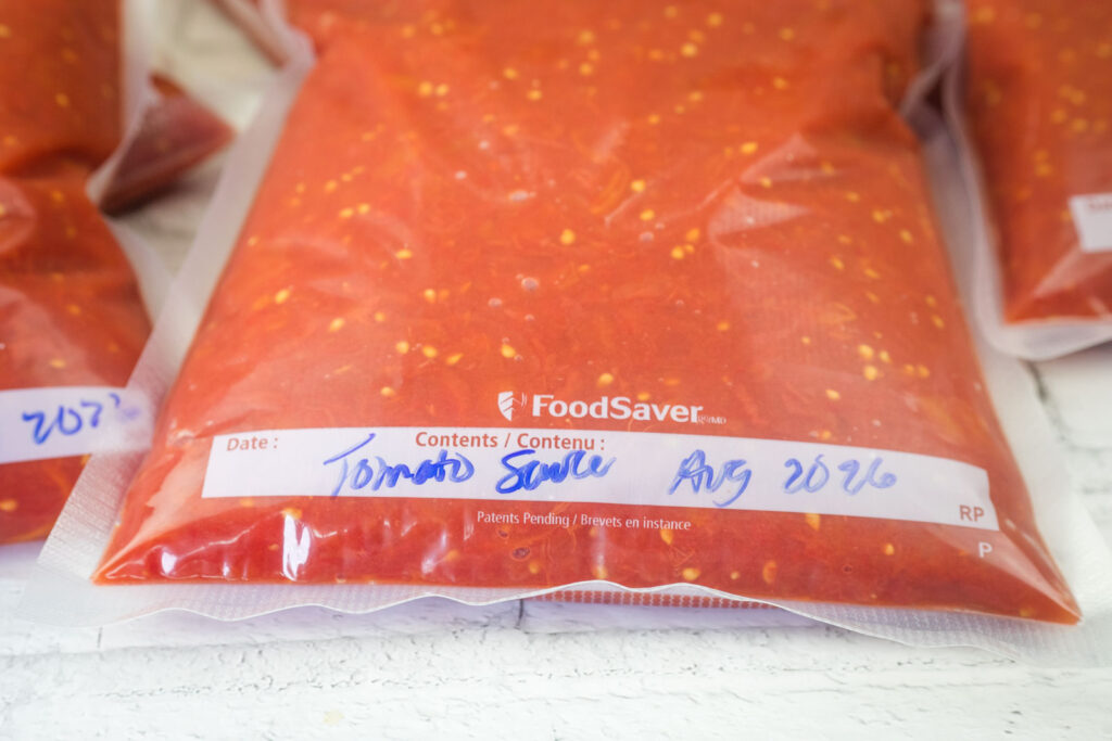 Vacuum-sealed bag of tomato sauce labeled with the date August 2026, placed on a white surface.