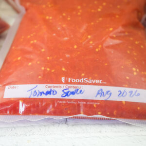 Vacuum-sealed bag of tomato sauce labeled with the date August 2026, placed on a white surface.