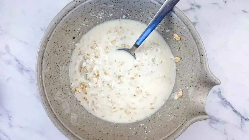 A speckled ceramic bowl containing oatmeal mixed with milk and a silver spoon.