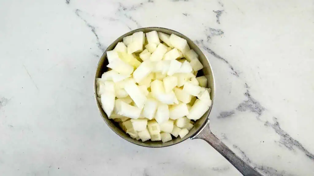 Small metal saucepan filled with chopped white onion.