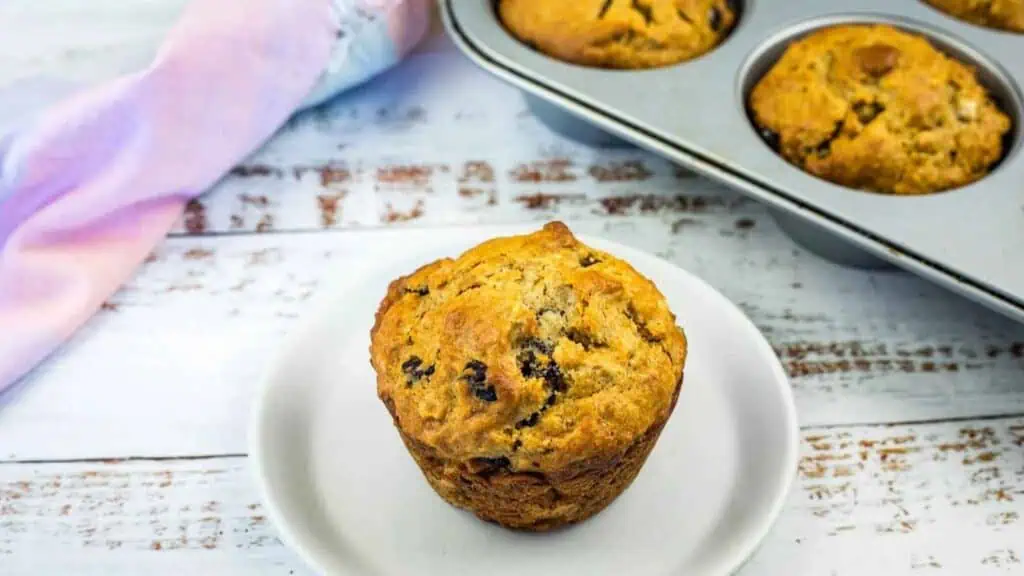 A freshly baked blueberry muffin on a small plate next to a muffin tin.