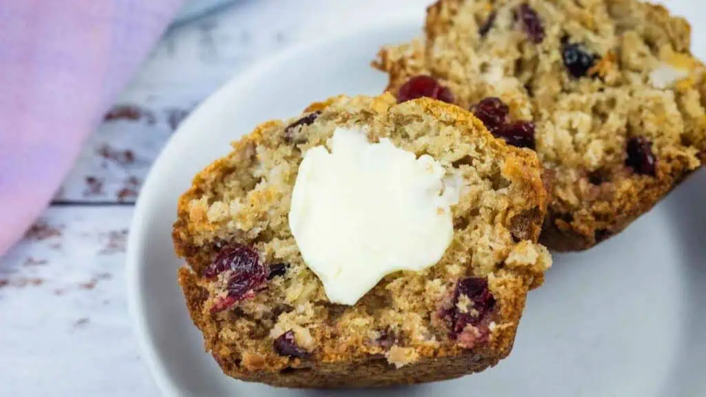 Two cranberry muffins on a plate, with a pat of melting butter on the front muffin.