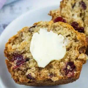 Two jumbo cranberry muffins on a plate, with a pat of melting butter on the front muffin.