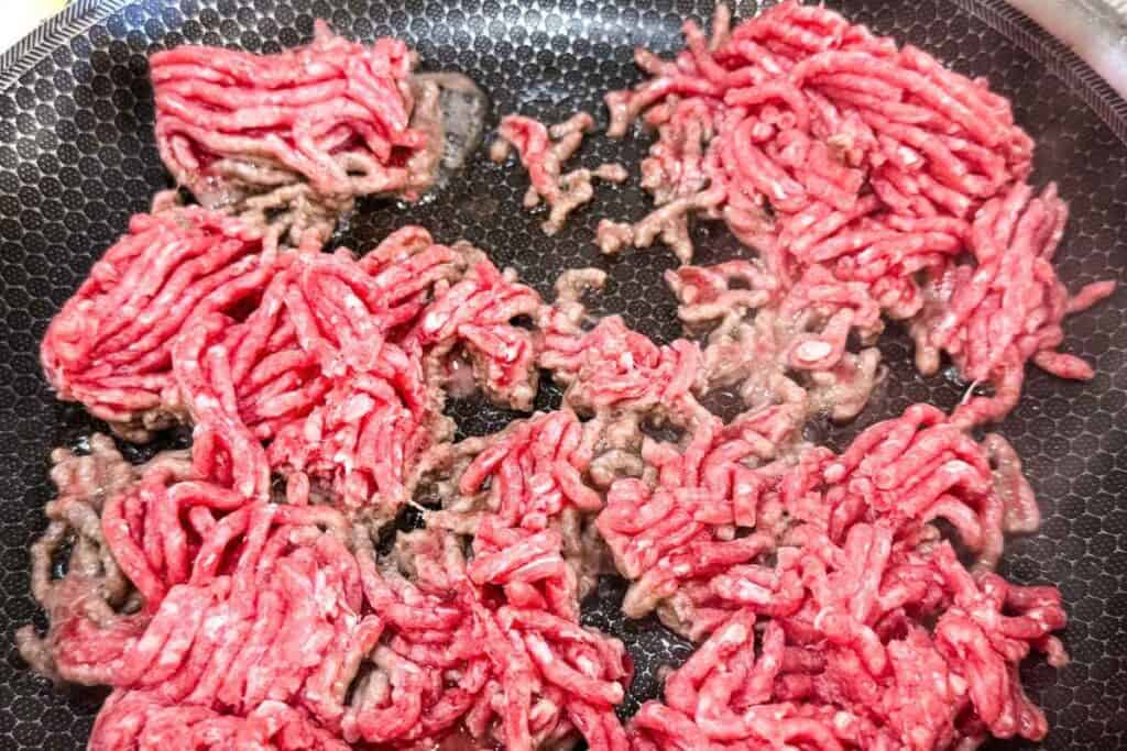 Ground meat browning in a textured frying pan.
