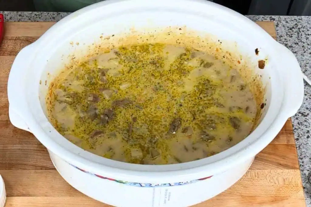 Creamy stew with meat and green herbs in a white ceramic slow cooker.