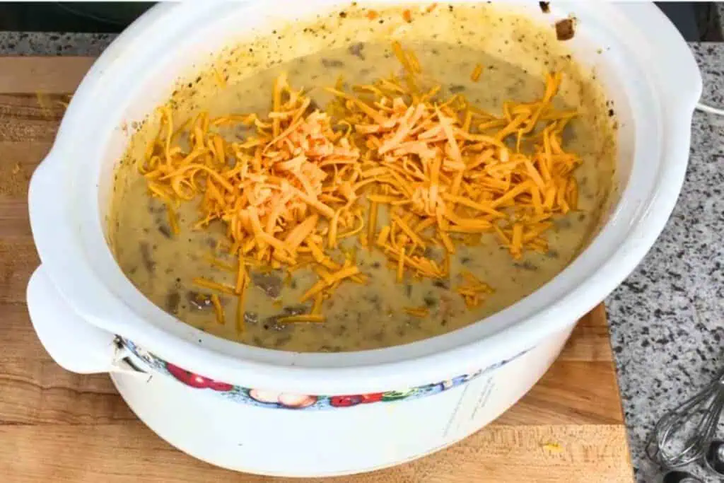 Creamy soup topped with shredded cheddar cheese in a slow cooker.