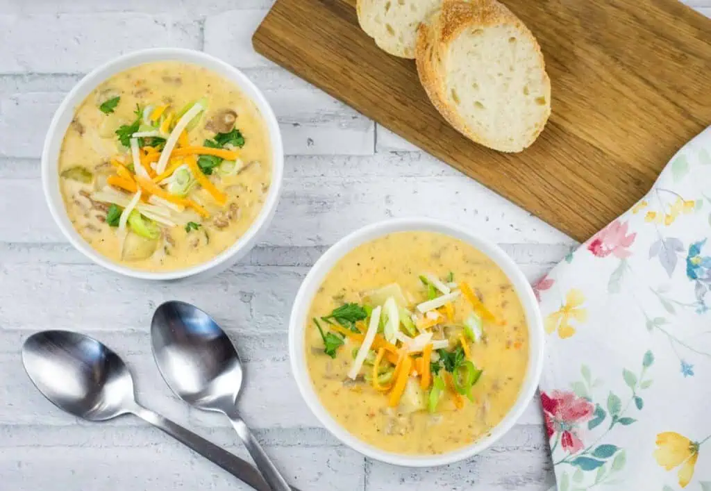 Two bowls of creamy soup topped with shredded cheese and green onions, served with slices of bread.