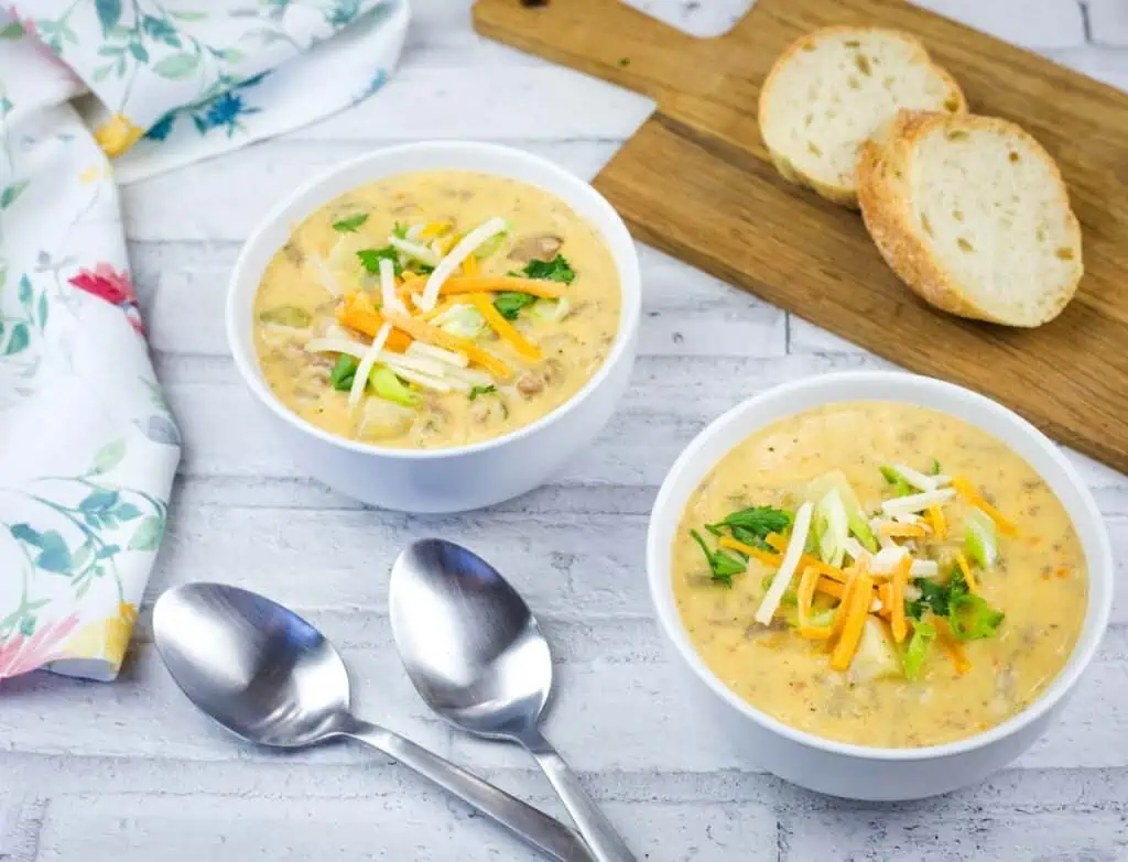 Two bowls of creamy potato soup topped with shredded cheese and green onions, served with two slices of bread.