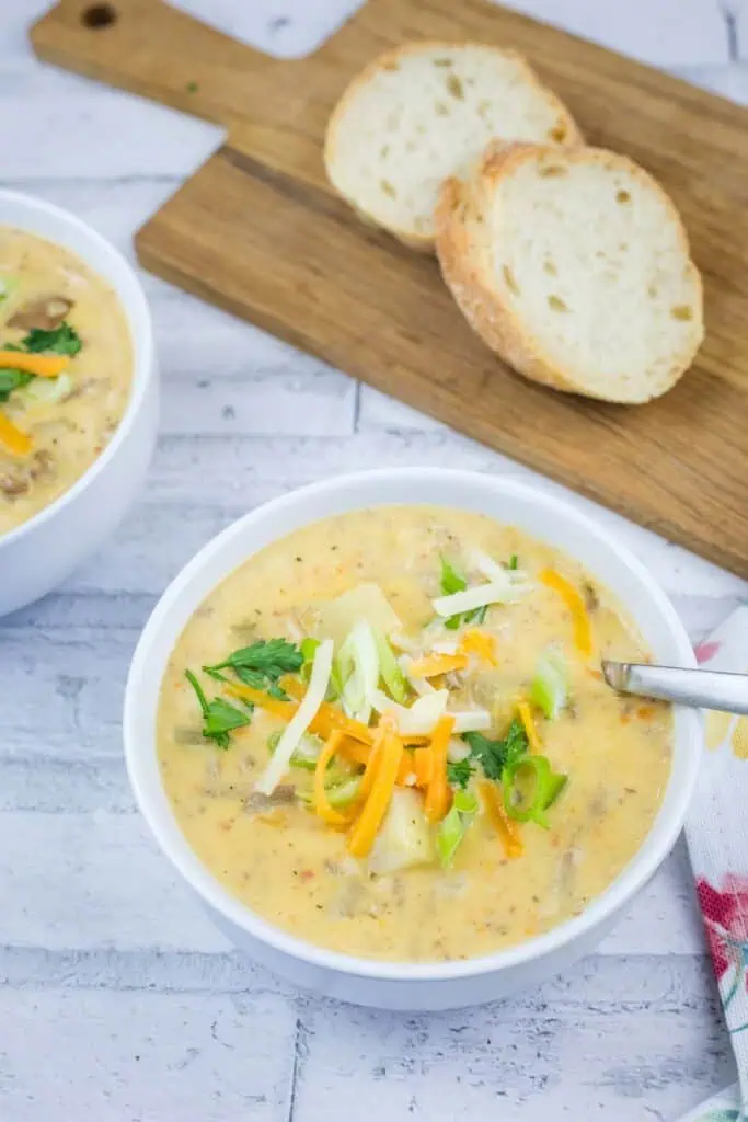 Two bowls of creamy potato soup topped with shredded cheese and green onions, served with sliced bread on a cutting board.